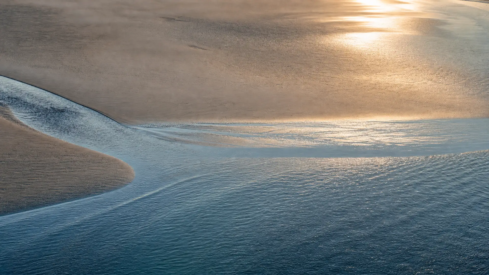 Golden morning light on the tide where it meets the sand.